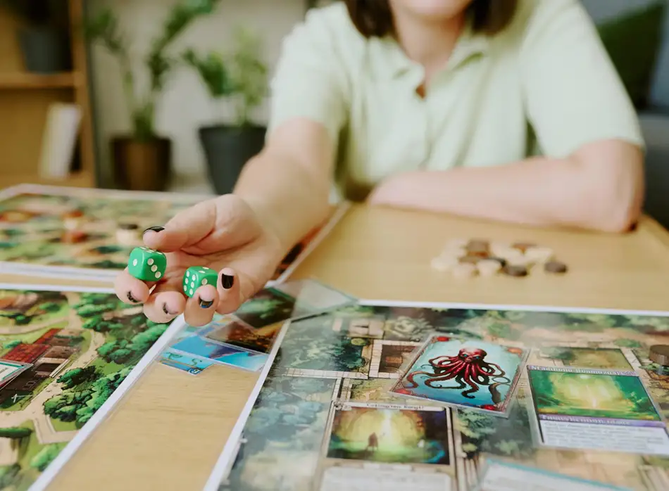Groene dobbelstenen met de hand rollen op een kleurrijk bordspel met kaarten en fiches.