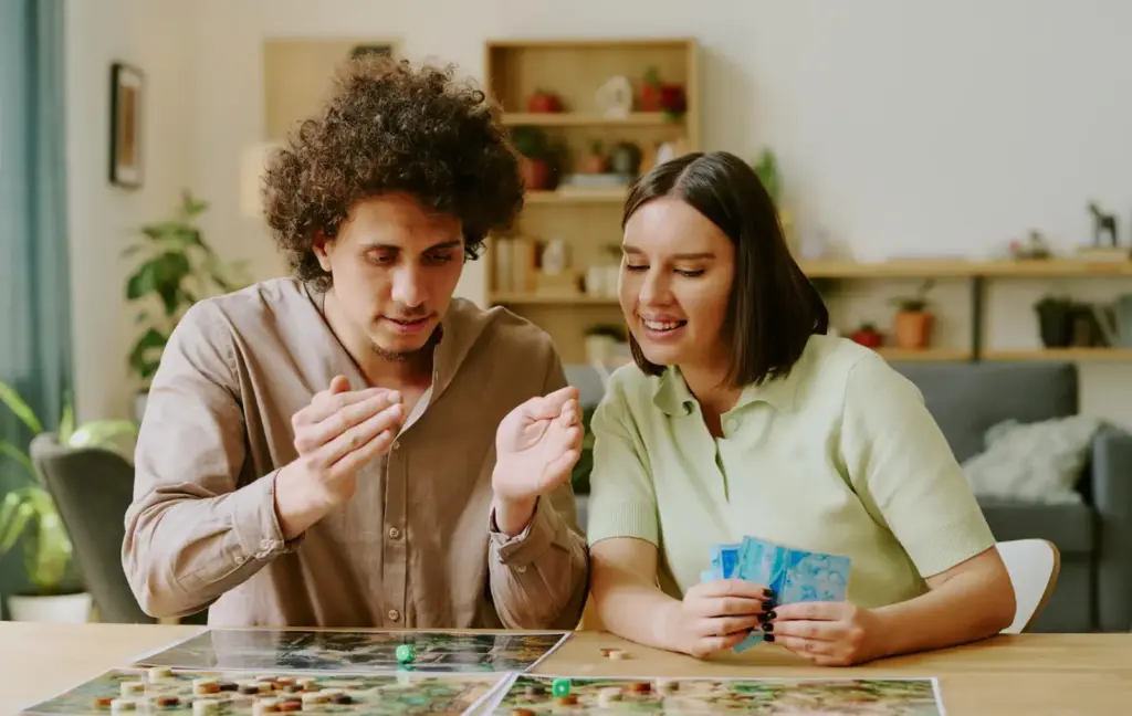 Twee vrienden die samen een bordspel spelen terwijl ze strategieën bespreken en speelkaarten vasthouden.